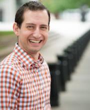 Dr. Seth Meyer looks at the camera and smiles in a red and blue checkered shirt outside