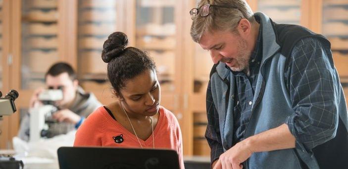 Professor Michael Krol showing something in a book to a student in geology lab