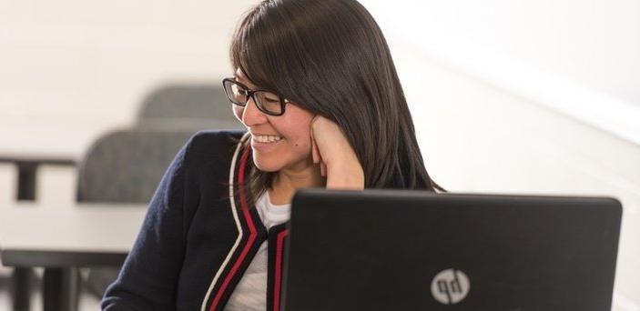 student at desk with laptop in class smiling